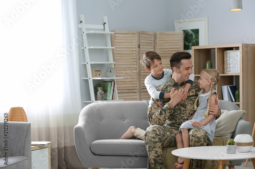 Young man in military uniform with his children on sofa at home photo