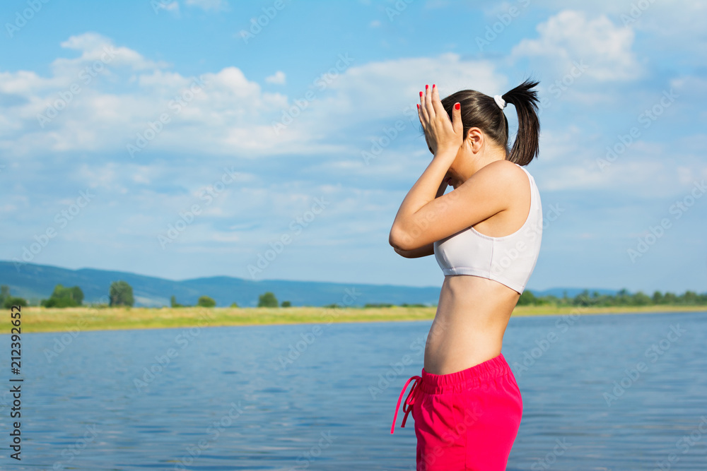 Tired young woman holding her head outdoors on the beach on sunny summer day. Female person with headache outside by the lake. No retouch, natural lighting. Tired young woman holding her head outdoors on the beach on sunny summer day. Female person with headache outside by the lake. No retouch, natural lighting.