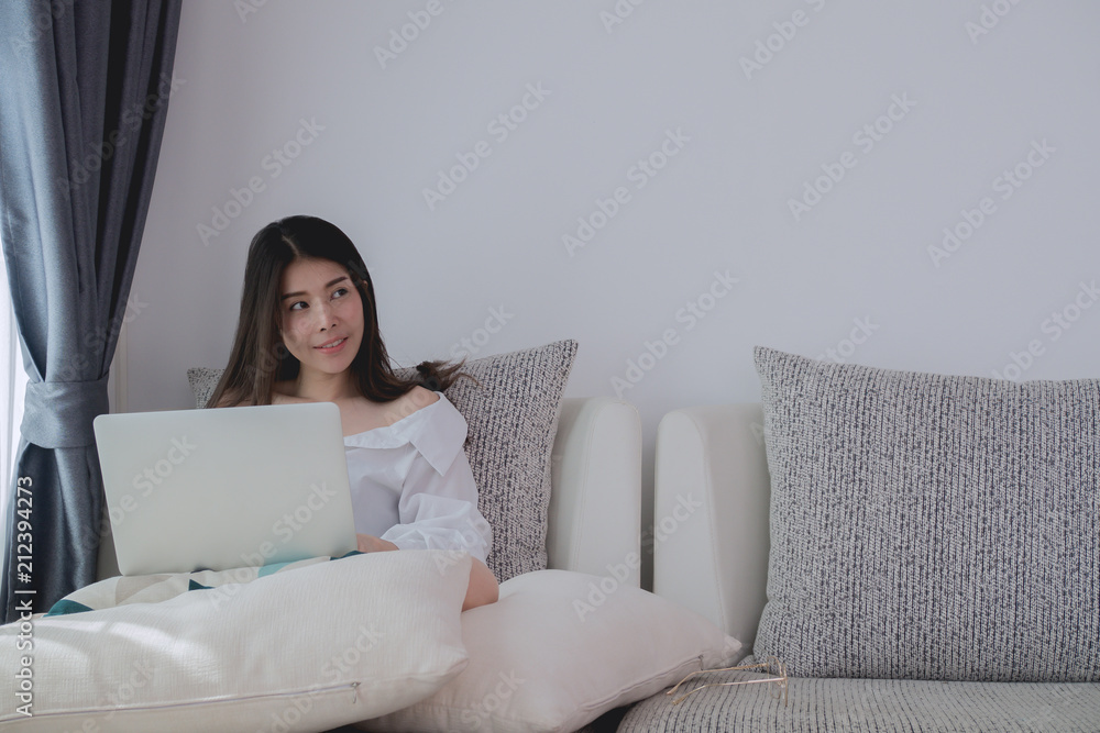 smiley face young asian woman thinking and using laptop, notebook on bed at living room. smiley face young asian woman thinking and using laptop, notebook on bed at living room.