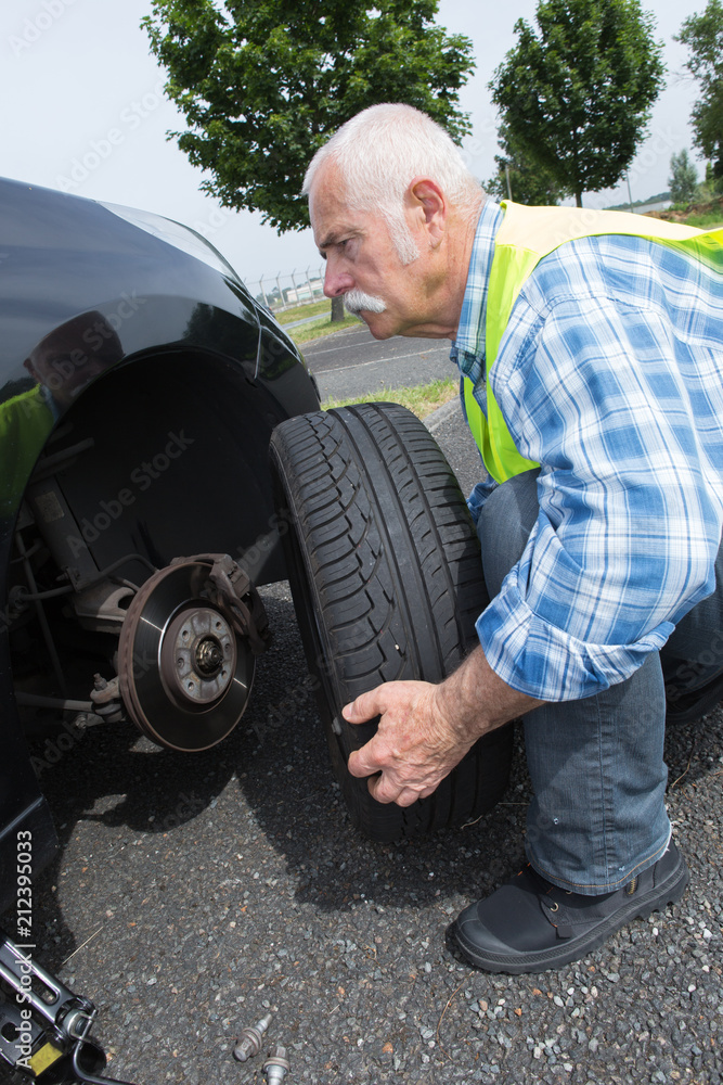 aged man changing leaking tire on the verge