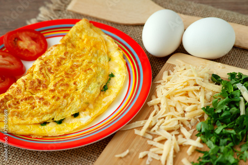 French omelette and its ingredients. French omelette on a bright saucer with an orange pattern. Breakfast of eggs, grated cheese and parsley in colorful tones.
