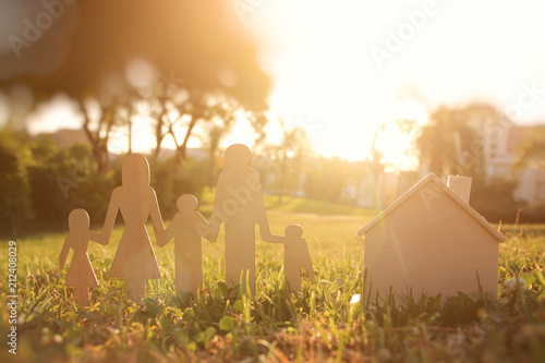 image of happy family concept. wooden cut people holding hands together next to home in green grass during sunset. photo