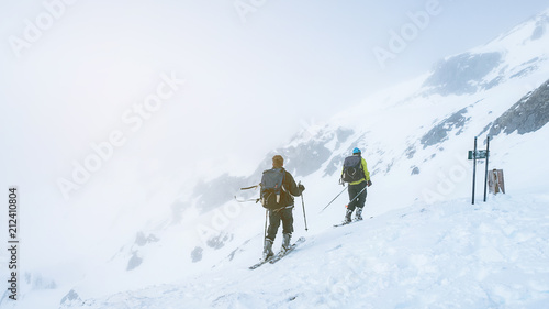 Two men skiing together on the snow mountains on a foggy day.