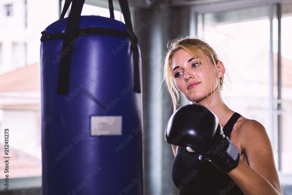 Young female punching a bag with boxing glove.