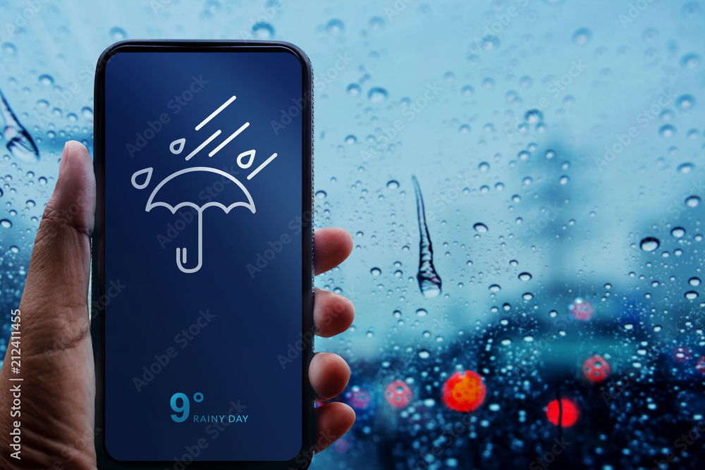 Rainy Day Concept. Hand Holding Smartphone with Weather Information show on Screen. Blurred Traffic Jam and Rain Drops on Glass Window as background - obrazy, fototapety, plakaty 