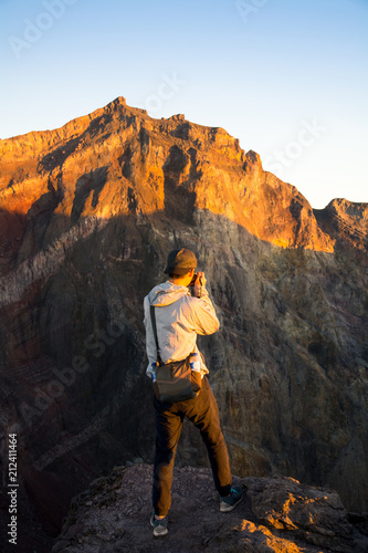 Young Traveler Man Taking A Photo On The Top of Mount Agung Volcano at Sunrise. Bali, Indonesia