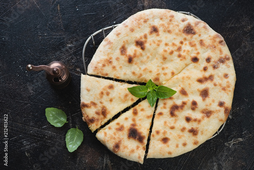 Ossetian pie with potato and cheese stuffing over dark brown stone background, flatlay, studio shot photo