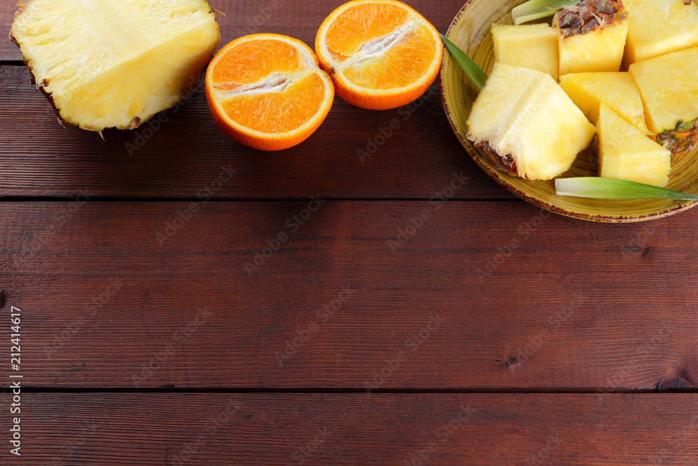 Pieces of pineapple and oranges on a yellow plate on wooden boards, pineapple and halves of orange on a wooden background, salad of tropical fruits for breakfast Pieces of pineapple and oranges on a yellow plate on wooden boards, pineapple and halves of orange on a wooden background, salad of tropical fruits for breakfast