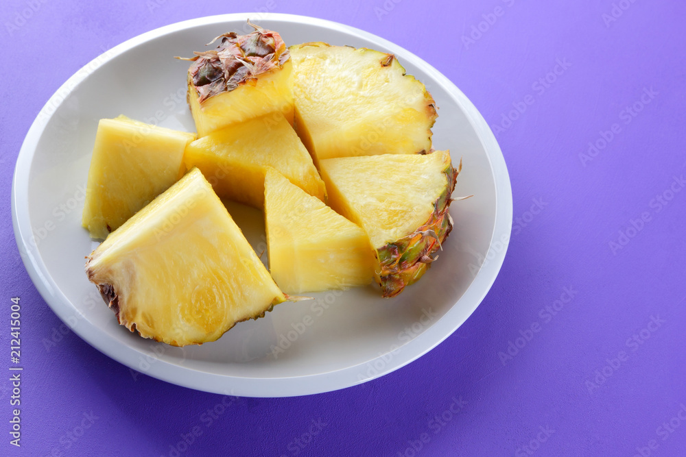Pieces of pineapple on a white plate, chopped fresh pineapple on a violet background, salad of tropical fruits for breakfast, Mexican food Pieces of pineapple on a white plate, chopped fresh pineapple on a violet background, salad of tropical fruits for breakfast, Mexican food