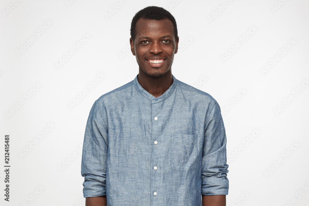 Horizontal shot of handsome African American man in blue shirt isolated on gray background standing, smiling happily and friendly as if encouraging communication Horizontal shot of handsome African American man in blue shirt isolated on gray background standing, smiling happily and friendly as if encouraging communication
