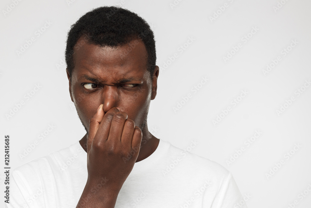 African american man in blank white tshirt, isolated on gray background holding his nose trying to escape from stinky smell and looking aside with worry looking for source of odor - obrazy, fototapety, plakaty 