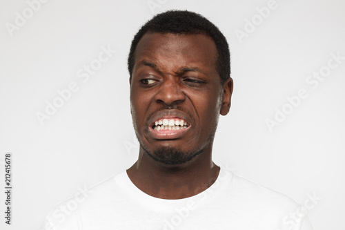 Disguting! Shocked young african american man in blank white t shirt looking at something unpleasant and bad, isolated on gray background. Negative emotion concept