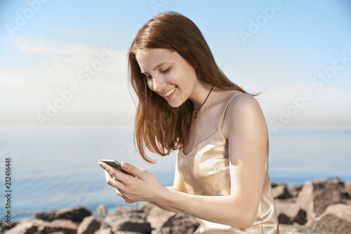 Young woman laughing and typing a message in the mobile Bay early morning. A girl with long red hair and a pleasant smile is blogging and personal life