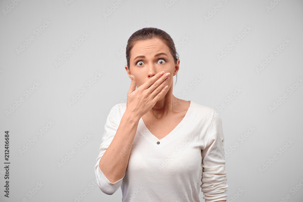Woman covering mouth not to tell secret of friend. Studio shot of shocked and amazed caucasian female student, holding palm on lip and staring with popped eyes at camera. People and reaction concept Woman covering mouth not to tell secret of friend. Studio shot of shocked and amazed caucasian female student, holding palm on lip and staring with popped eyes at camera. People and reaction concept