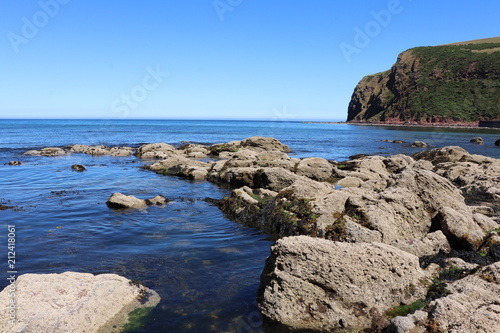 Close up of rocks by sea in foreground with sea and cliffs beyond © mcKensa