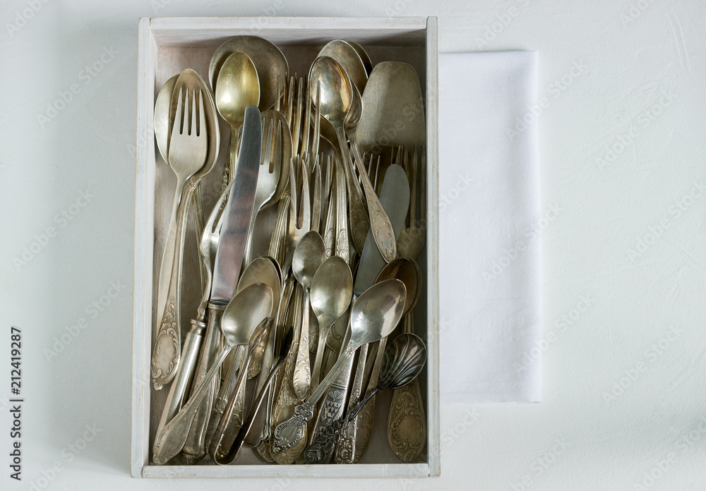 Vintage silver cutlery in a white wooden box on a white table. Rustic style.