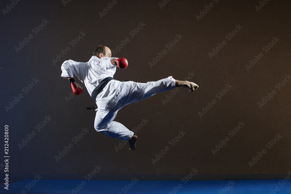 An athlete with a black belt trains a kick leg in a jump