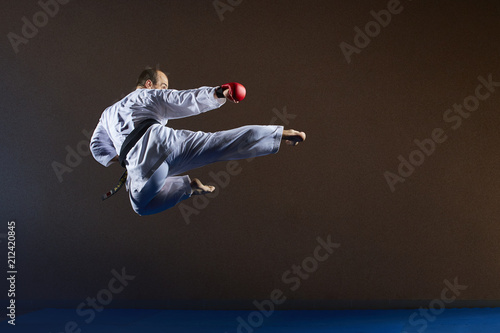 A man with a black belt trains a kick in a jump