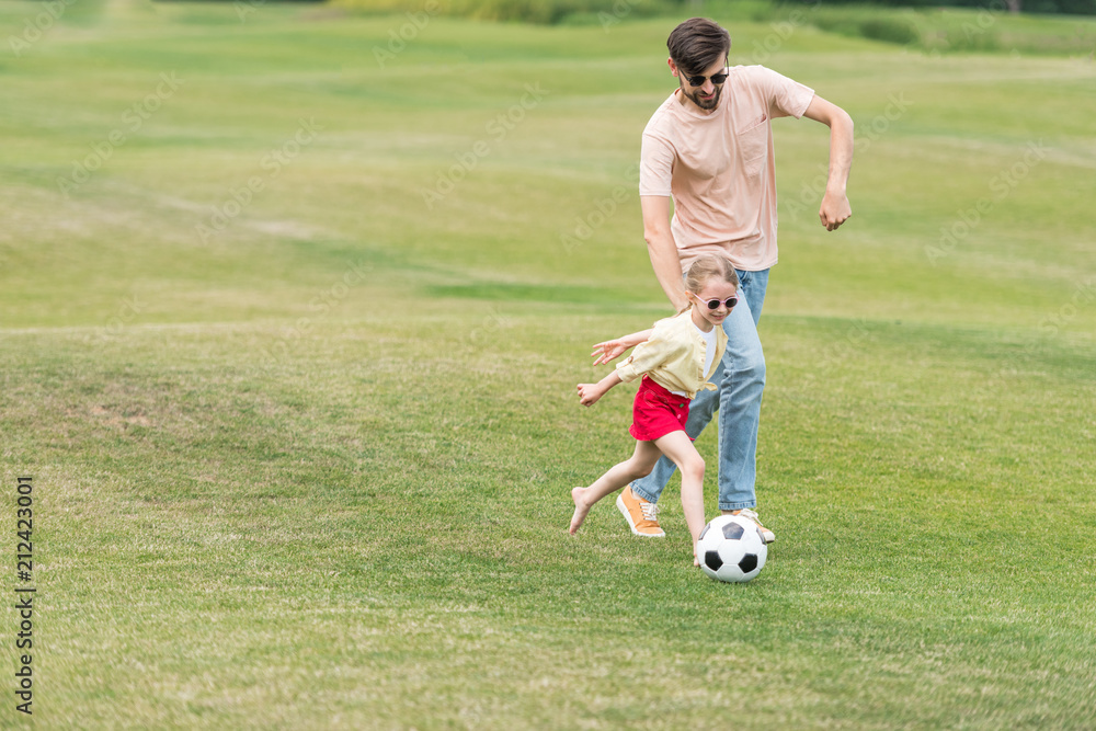 happy father and little daughter playing with soccer ball in park