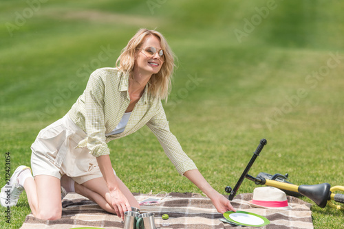 happy young woman putting cutlery on plaid at picnic © LIGHTFIELD STUDIOS