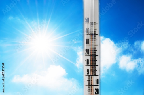 Thermometer against the background of an blue hot glow of clouds and sun, concept of hot weather. Above 40 degrees Celsius.