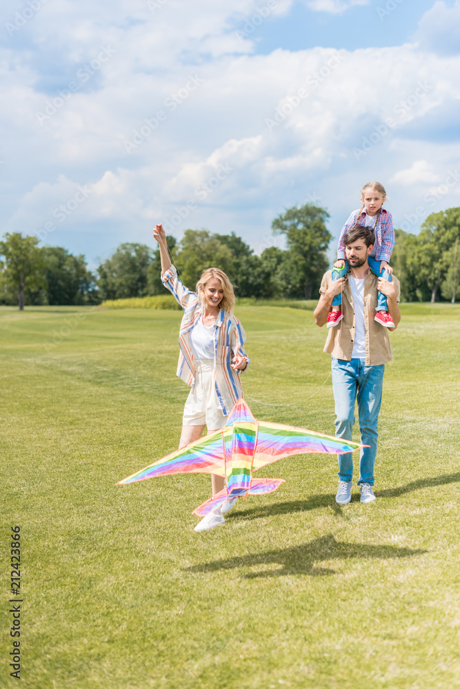 Fototapeta premium happy young parents and cute little daughter playing with colorful kite in park