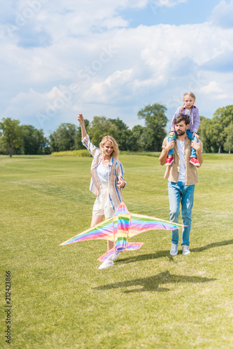 happy young parents and cute little daughter playing with colorful kite in park