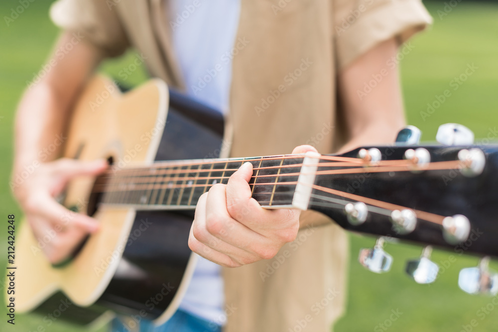 cropped shot of man playing acoustic guitar in park