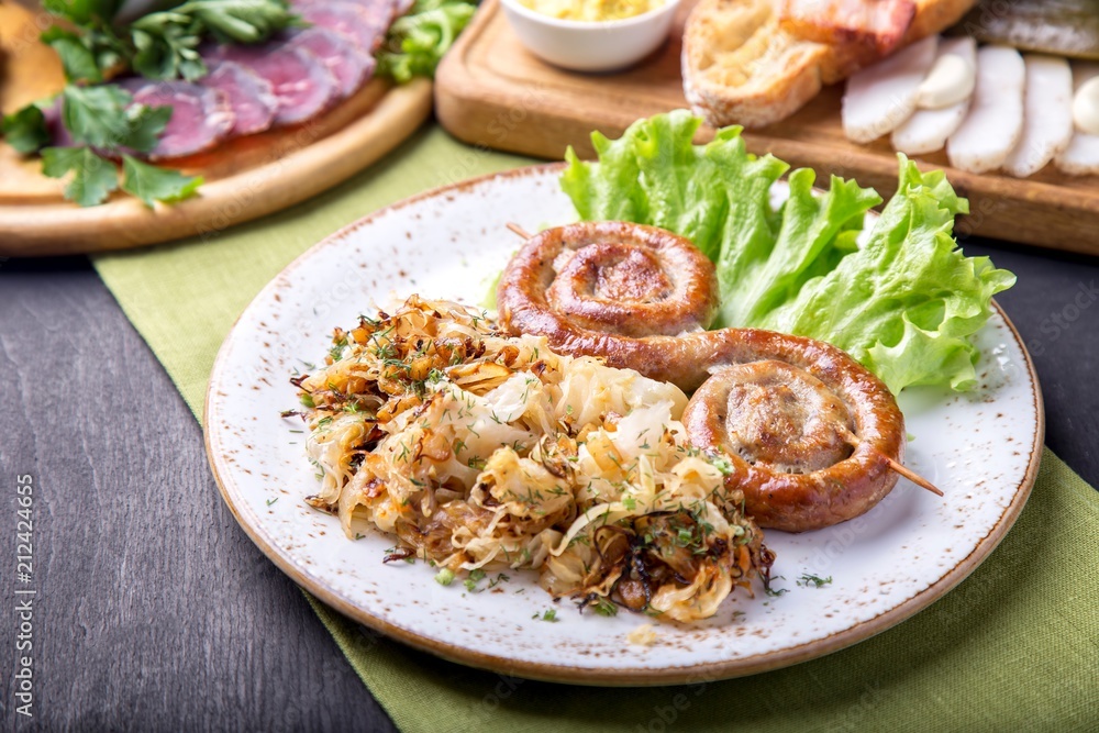 Tasty round roast sausages on wooden skewers with fried sauerkraut Tasty round roast sausages on wooden skewers with fried sauerkraut