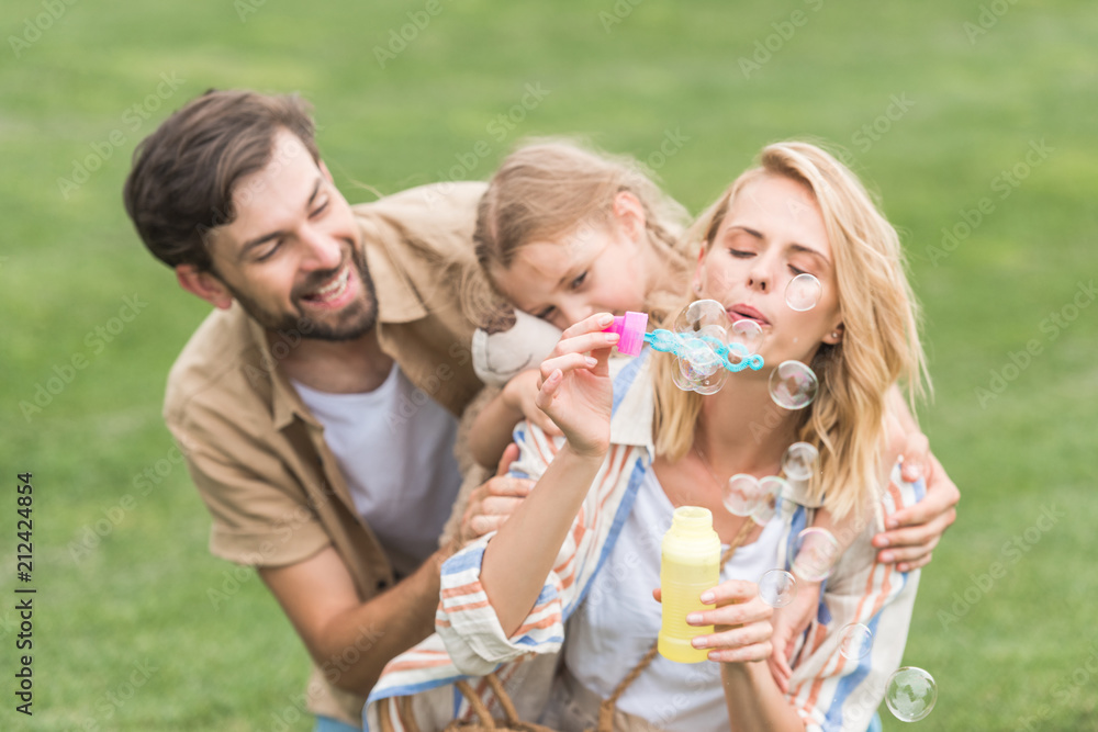 happy family with one child having fun together and blowing soap bubbles in park