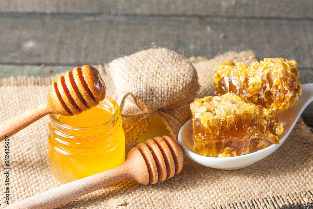 Honey dripping from a wooden honey dipper in a jar on wooden grey rustic background Honey dripping from a wooden honey dipper in a jar on wooden grey rustic background