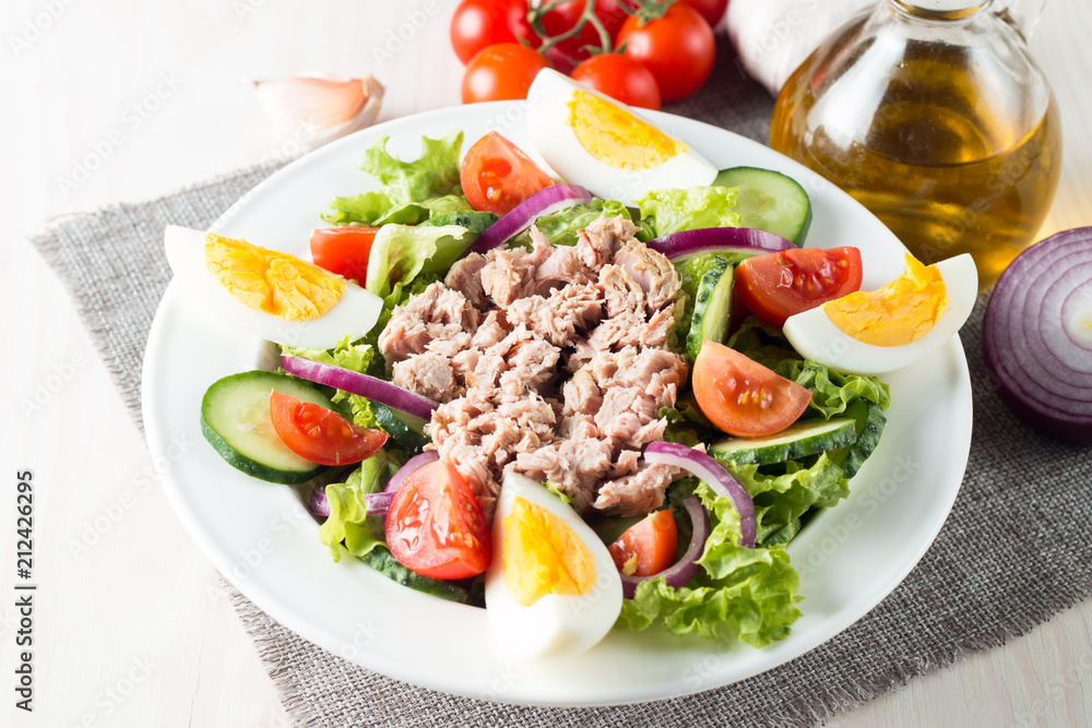 Fresh fish tuna salad made of tomato, ruccola, tuna, eggs, arugula, crackers and spices. Caesar salad in a white bowl on wooden background