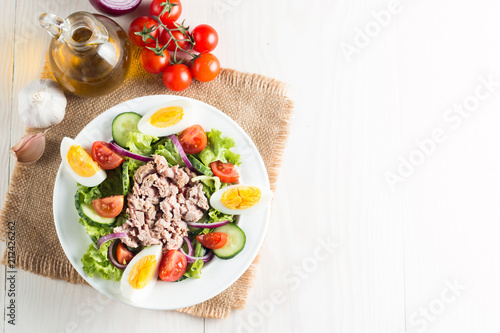 Fresh fish tuna salad made of tomato, ruccola, tuna, eggs, arugula, crackers and spices. Caesar salad in a white bowl on wooden background