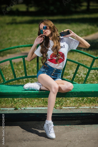 Young beautiful girl listening to music in headphones, sitting on a bench