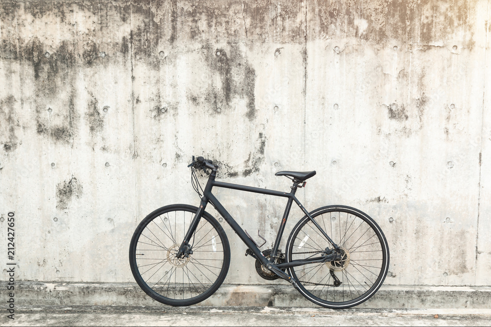 Matt black race road bike parked in front of grunge textured background with vintage tone.
