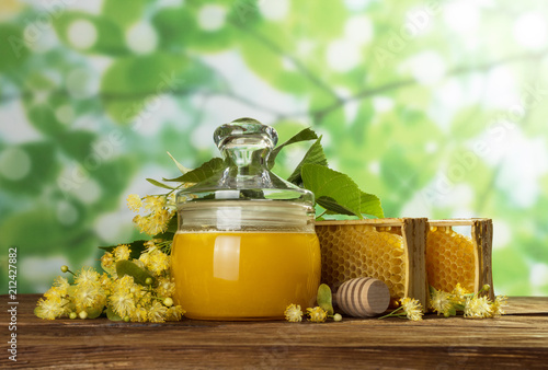 Honey in pot with lid, honeycomb and spoon on green background
