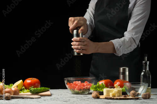 The chef prepares a salad, with a Pepper mill on a dark background with an empty space for writing