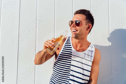 Bilde på lerret Cheerful attractive man in sunglasses drinking cold beer, enjoying hot summer days, outside