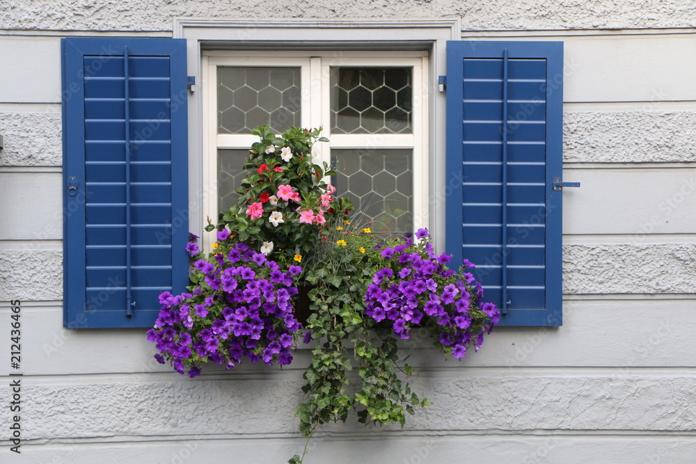 Blue Window with Flowers, blaues Fenster mit Blumenschmuck, traditionelles Fenster im Alpenraum