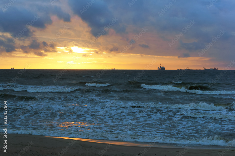 Sunset on the sea. The waves beat against the breakwater. The sea at dawn. The ships on the horizon.