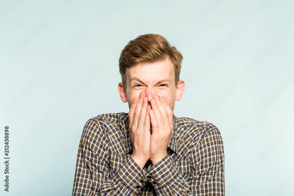 joyful excited happy smiling man covering mouth with hands. portrait of a young guy on light background. emotion facial expression. feelings and people reaction. joyful excited happy smiling man covering mouth with hands. portrait of a young guy on light background. emotion facial expression. feelings and people reaction.