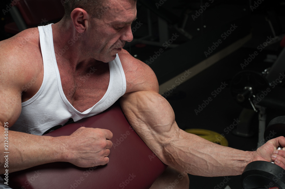 Portrait of mature fitness model working out with dumbbells. Strong muscular bodybuilder training in gym. Portrait of mature fitness model working out with dumbbells. Strong muscular bodybuilder training in gym.