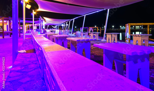 view through the railing and waterfront cafes at night shore with bright colors  Crete  Greece