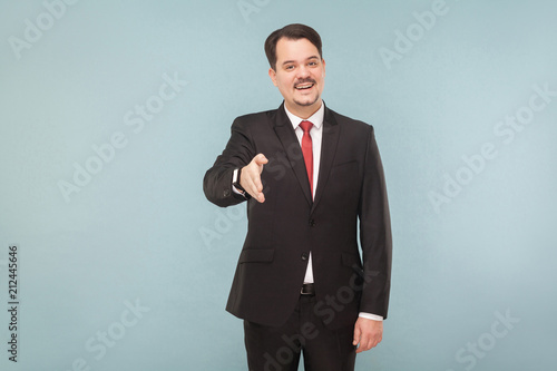 Congratulations you are hired, you will have your office and assistant. indoor studio shot. isolated on blue background. handsome businessman with black suit, red tie and mustache looking at camera.