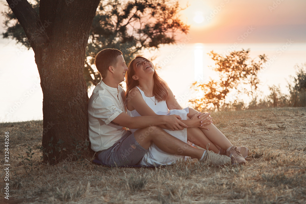 A beautiful couple in love sit under a tree at dawn. Happy relationship of a guy and a girl. A beautiful couple in love sit under a tree at dawn. Happy relationship of a guy and a girl.