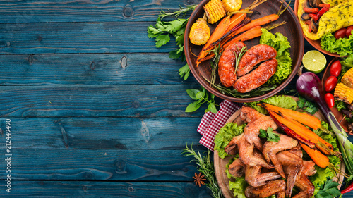Food. Grill sausages and chicken wings with vegetables. On a wooden background. Top view. Copy space.