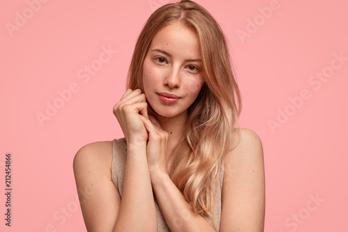 Cute young female model holds hands together near face, has pure healthy skin...