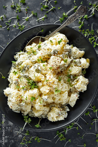 Warm potato salad with gherkins in a black plate photo