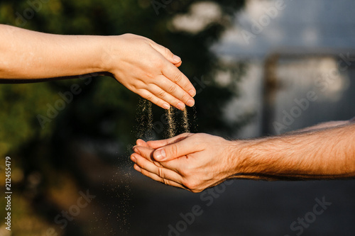 The sand is poured from the female hands into the masculine hands.