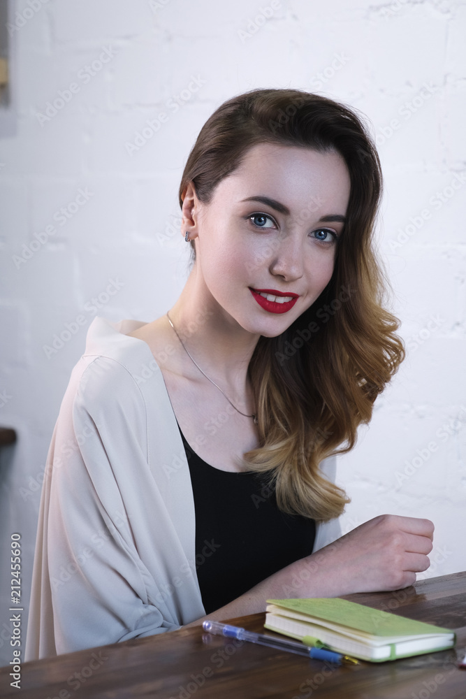 A beautiful girl with loose curls and red lips sitting at a table with a notebook. A beautiful girl with loose curls and red lips sitting at a table with a notebook.